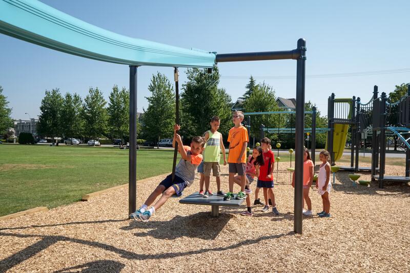 A child rides on a Zipkrooz track ride seat while several children look on from platform