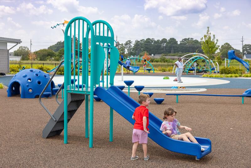 Young girl at the bottom of a freestanding playground slide with a boy nearby