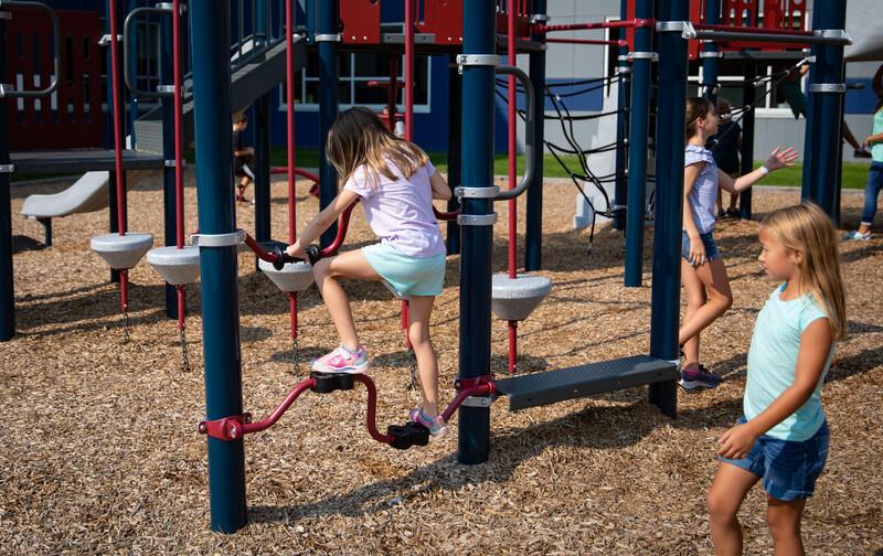 Girl in jean shorts watches friend in purple shirt riding Stationary Cycler