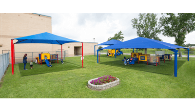 Childcare-aged kids playing on primary-colored playground equipment. Three separate playground areas covered by blue shade.