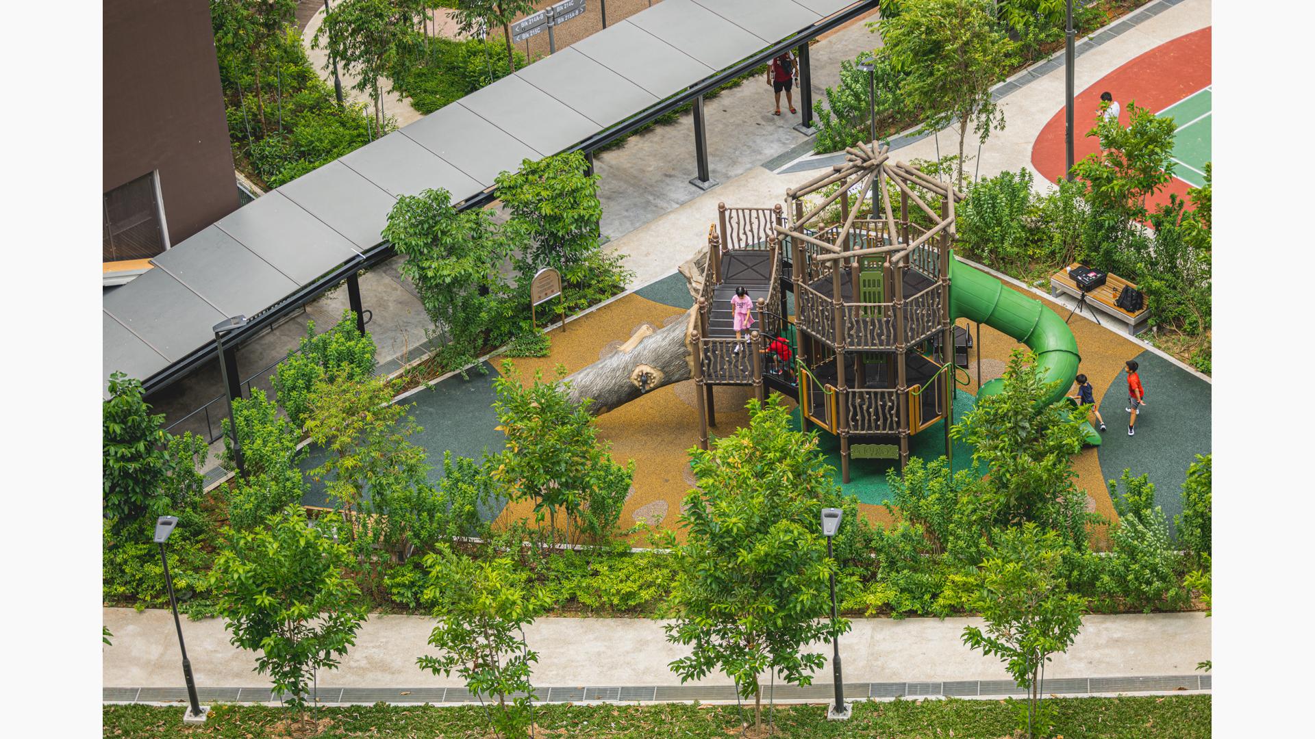 Elevated view of a park playground where the barriers and posts of a two story tower look like natural log sticks and a large log inspired slide.