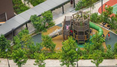 Elevated view of a park playground where the barriers and posts of a two story tower look like natural log sticks and a large log inspired slide.