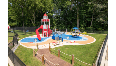 A beach themed play area with light house tower structure with safety surfacing designed like water and sandy beach with footprints.