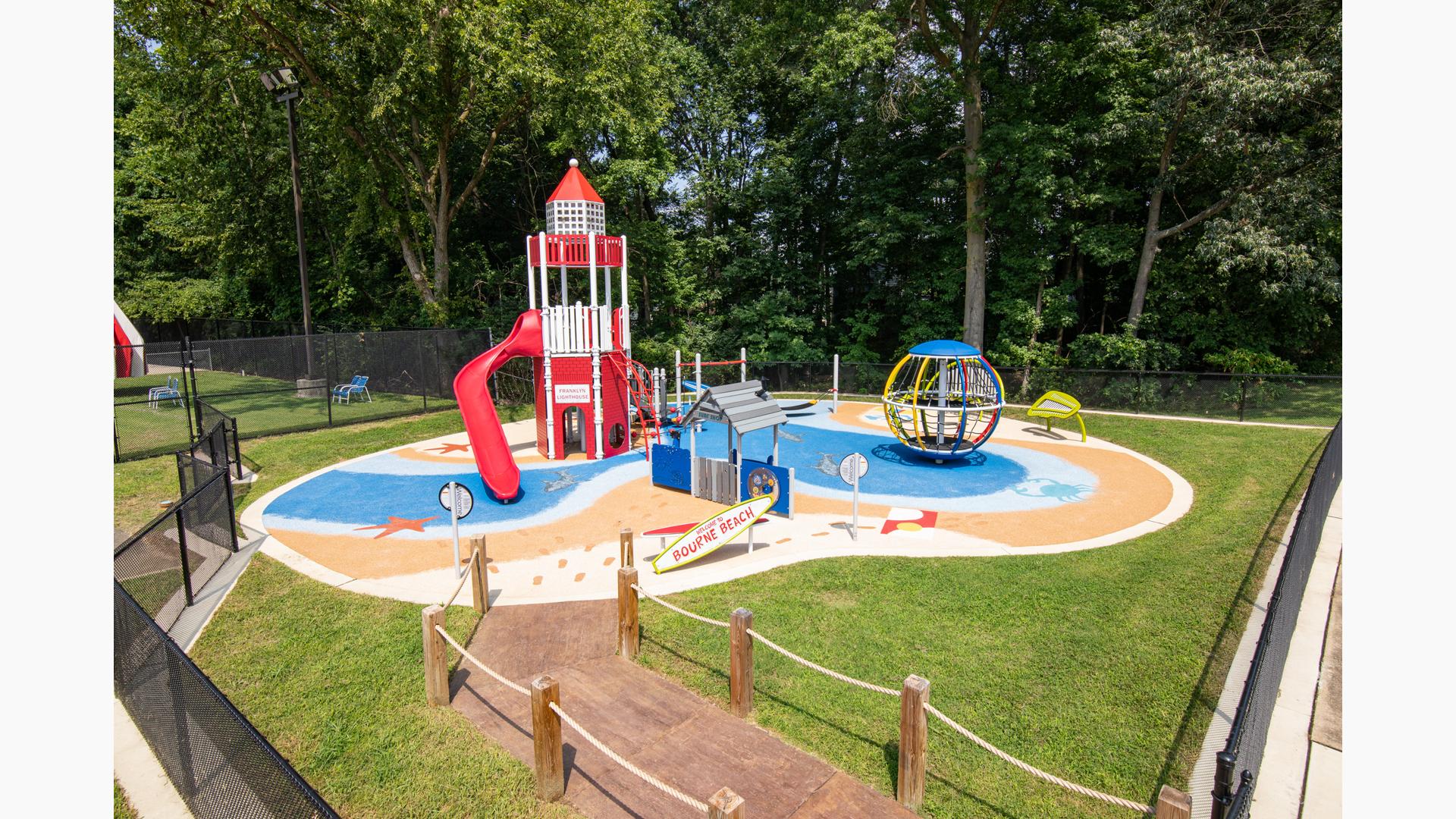 A beach themed play area with light house tower structure with safety surfacing designed like water and sandy beach with footprints.