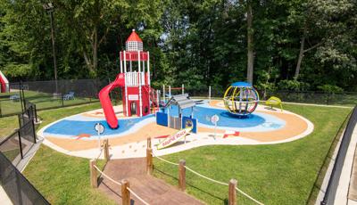 A beach themed play area with light house tower structure with safety surfacing designed like water and sandy beach with footprints.