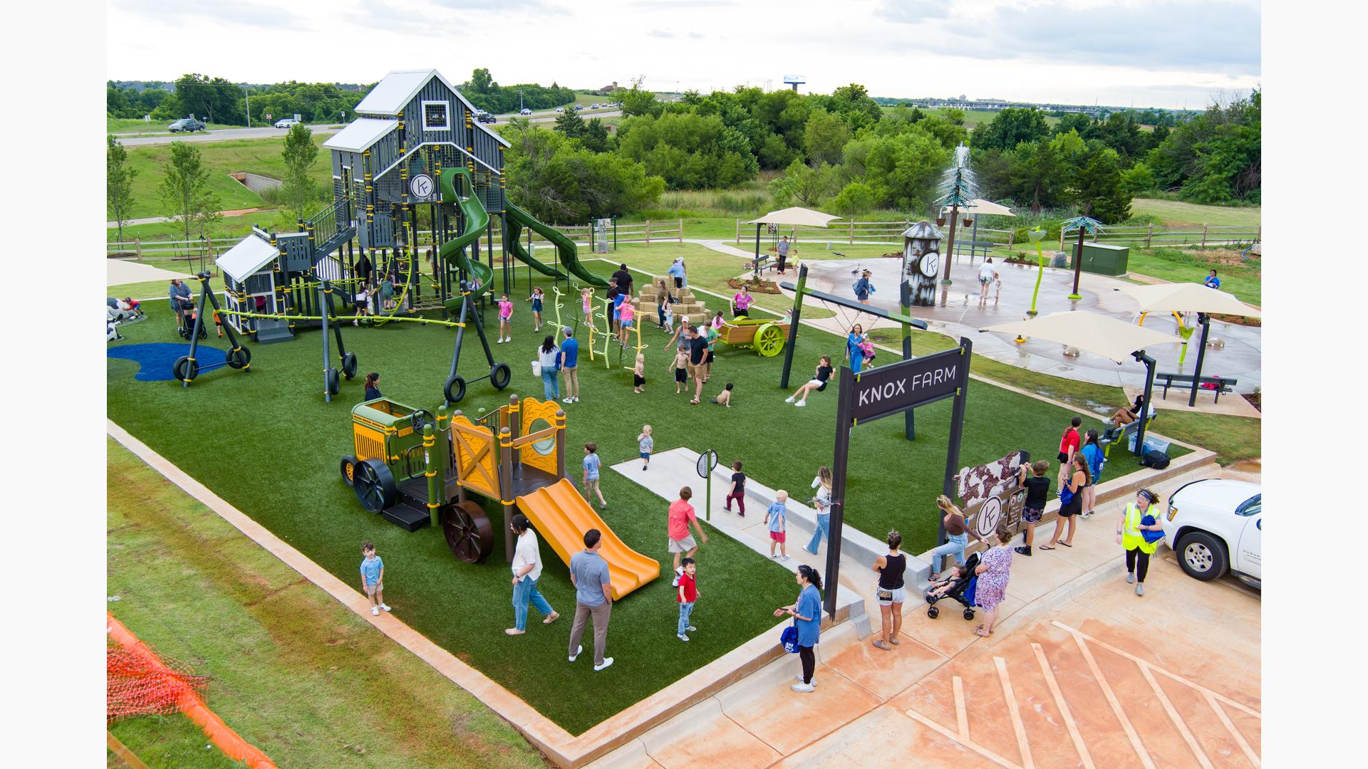 Elevated view of families playing at a farm themed playground next to a splash pad.