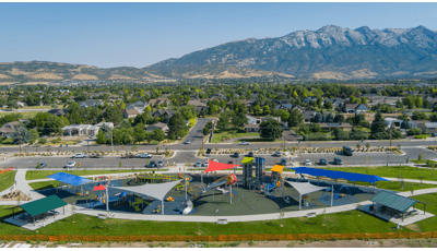 Elevated view of a large football shaped play area with unique play towers and other activities with a mountain range in the background.