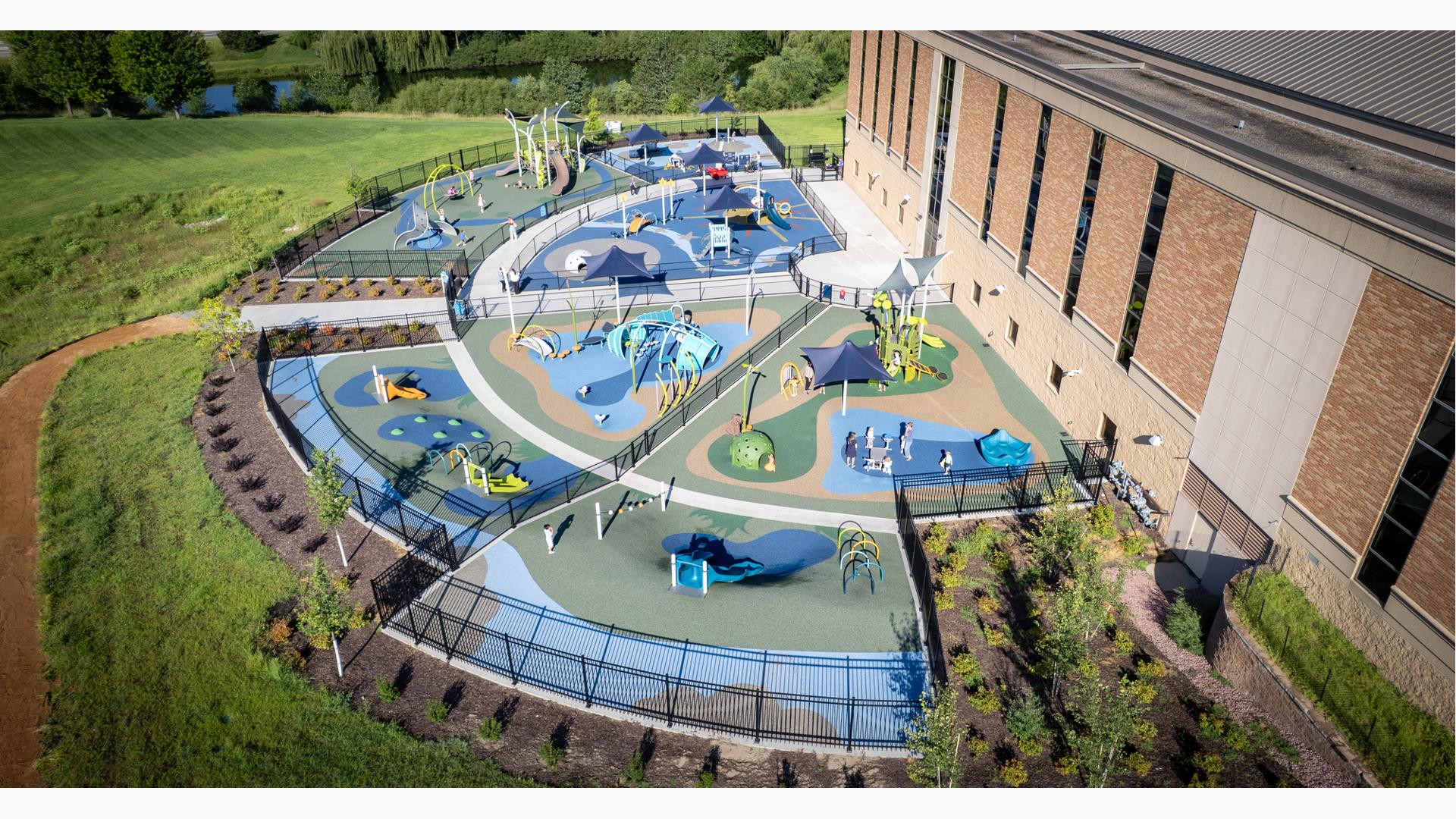 Elevated view of a large half moon shaped play area divided by fencing for specific play areas based on age designed with a religious theme of the creation of the world.