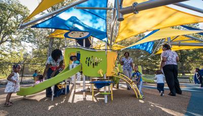Teachers help these toddlers play on a Smart Play play structure. A girl in a white dress stands at the foot a the Smart Play slide as two children ride down with their teacher's help.