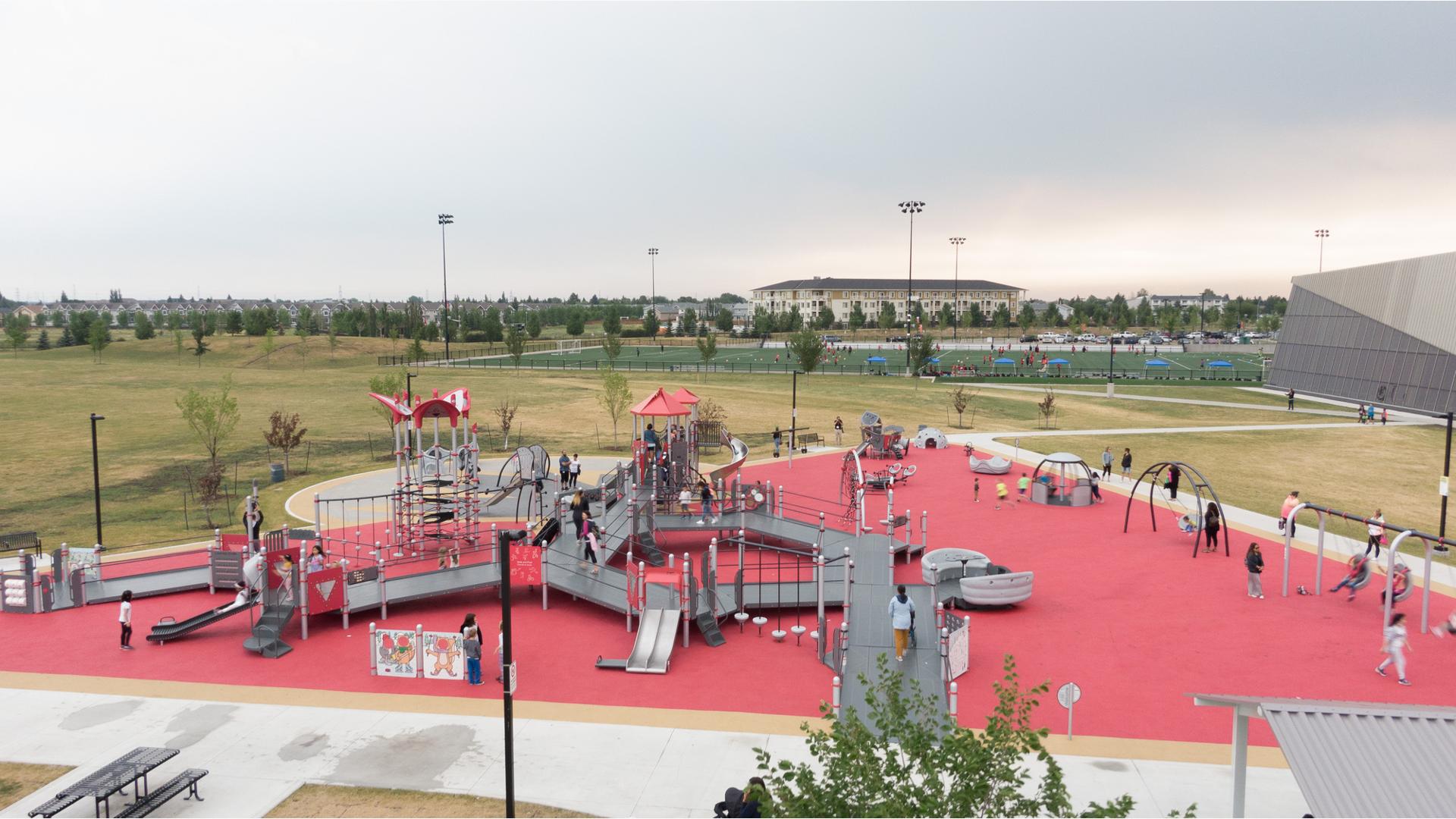 Elevated view of a triangular shape play area. One large play structure is connected by accessible ramps and bridges for all abilities. Swing sets and other accessible playground activities sit on the perimeter of the play area.