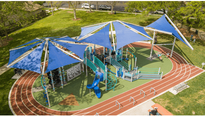 A running track surrounds a large inclusive playground with three large shade systems overhead.