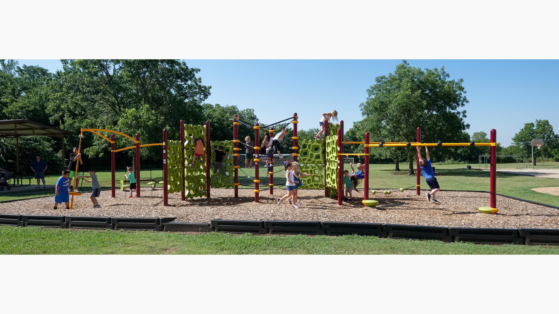 Children play on a continious play structure connected with spinners, climbers, and monkey bars at a park playground.