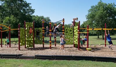 Children play on a continious play structure connected with spinners, climbers, and monkey bars at a park playground.