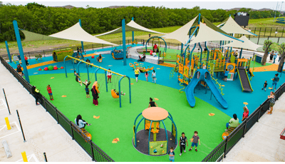 Families play at an inclusive playground with multiple accessible playground structures and over head shade sales.