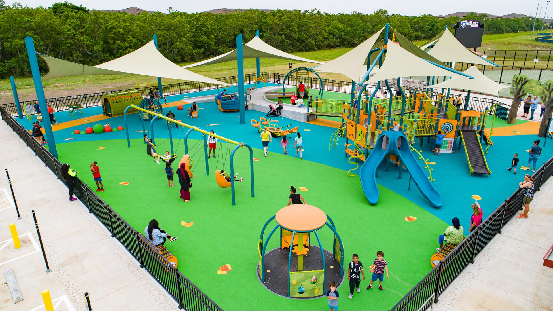 Families play at an inclusive playground with multiple accessible playground structures and over head shade sales.