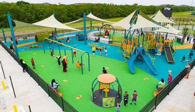 Families play at an inclusive playground with multiple accessible playground structures and over head shade sales.