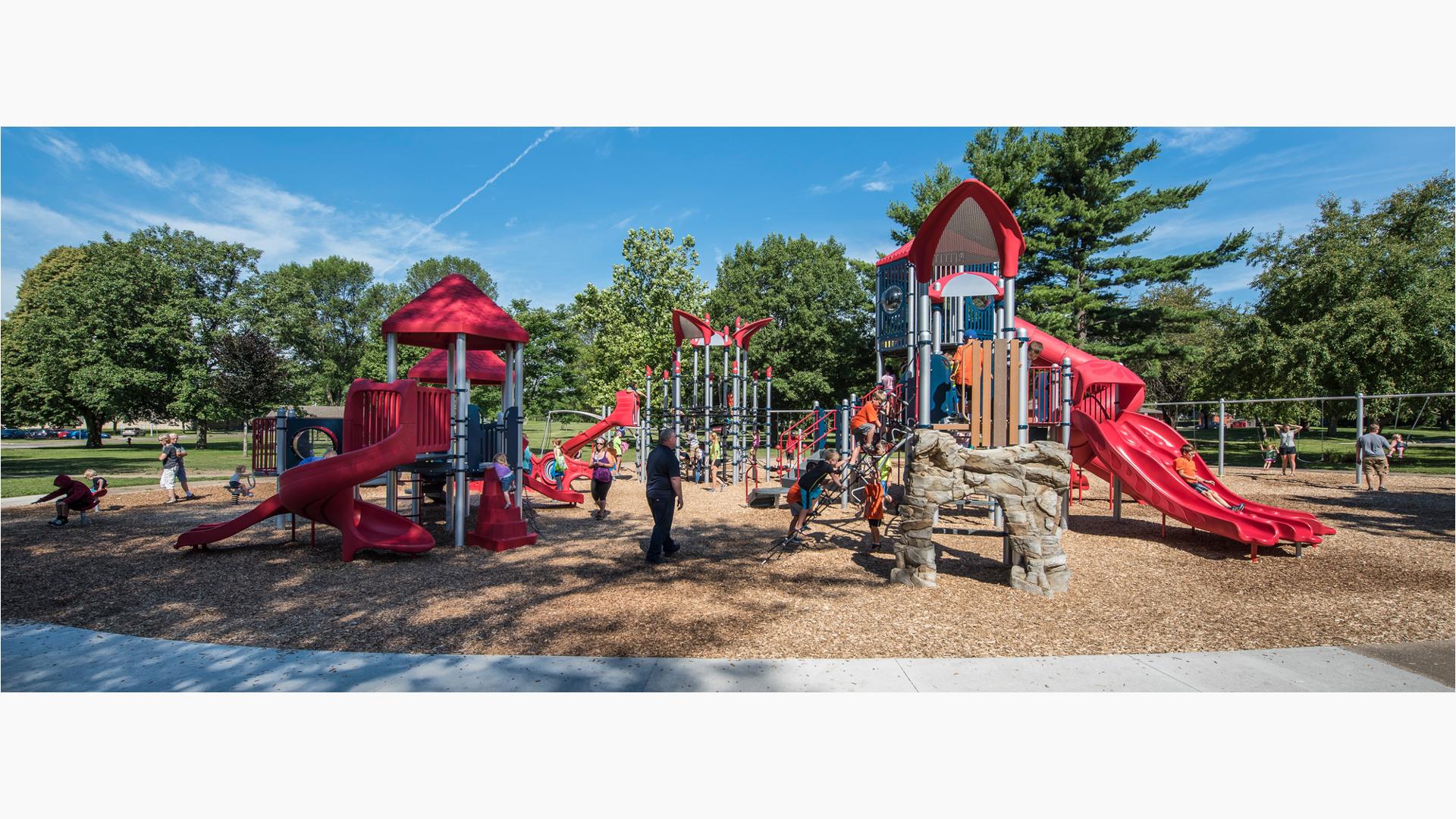 Kids can climb, swing, twirl and slide on a PlayBooster® play structure while an adult in black watches. The Geo Netplex in the background is covered with children at the base.