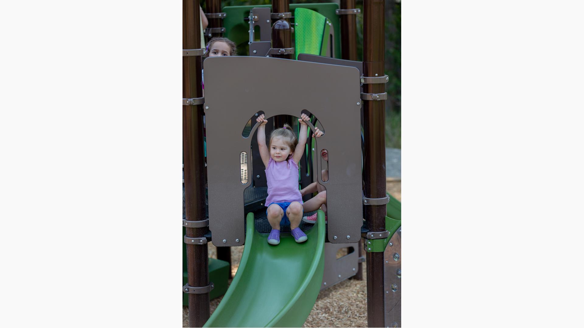 Girl sitting on top of Play shaper slide.