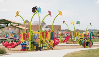 New custom Spring-themed playground with big flowers towering over the play structures, reaching up toward the sky. Bug, Bee, and catapillar-themed details add life.