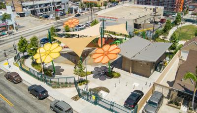 Elevated view of daisy designed shade systems with triangular shade sails cover a large play area of a splash pad and playground in a town center.