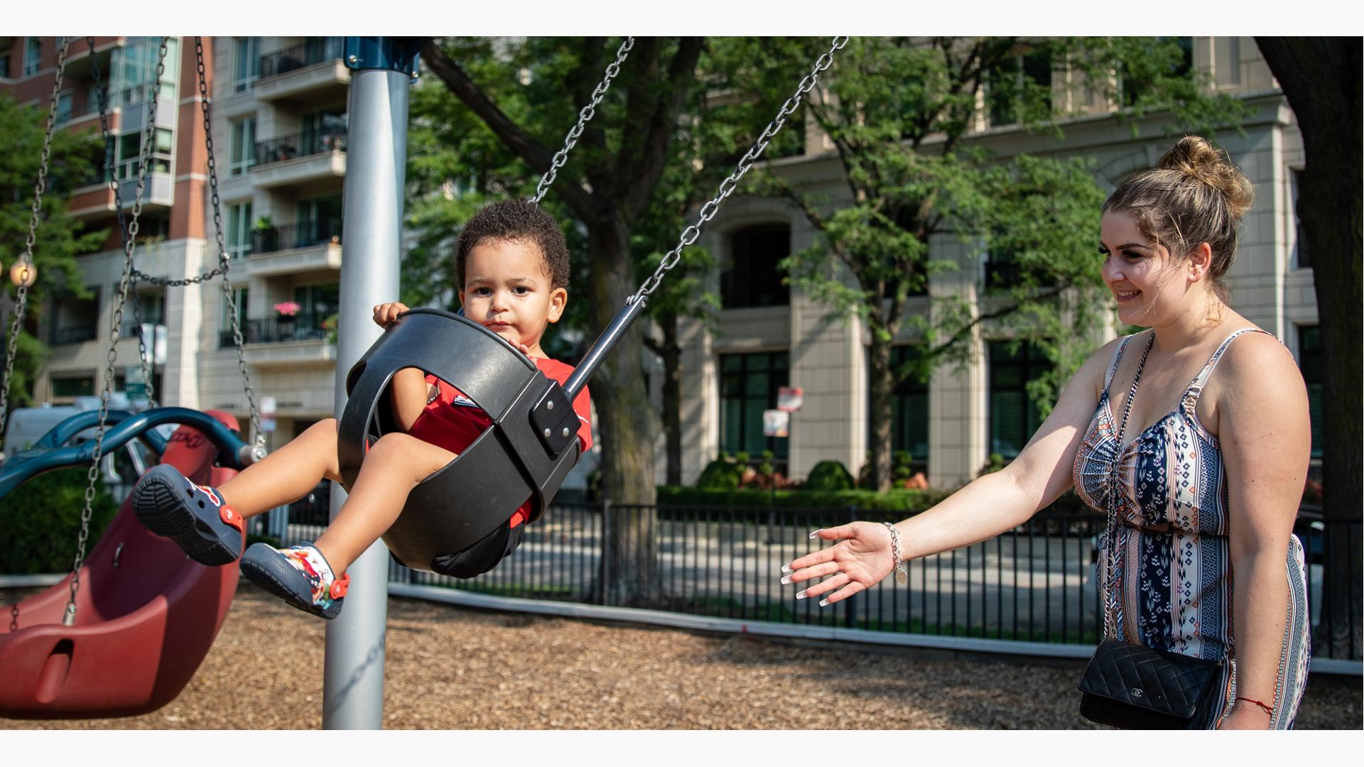 Boy in full bucket booster swing being pushed by mom