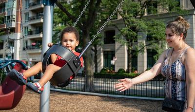 Boy in full bucket booster swing being pushed by mom