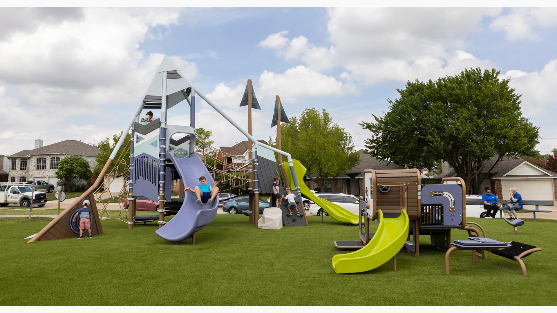 Children play on a mountain themed play structure at an neighborhood park with an additional smaller play structure for younger children with similar color scheme.