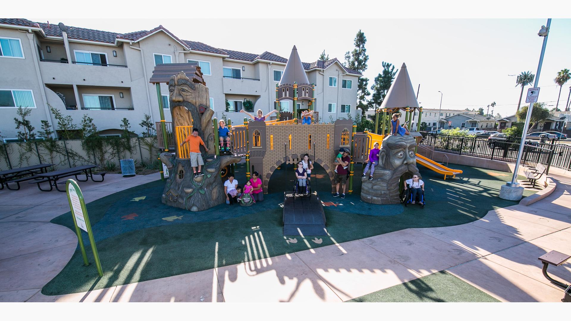 An custom all inclusive play structure disguised as a castle with ramp acting as a lowered draw bridge. Children of all ages and abilities gather and pose for a photo.