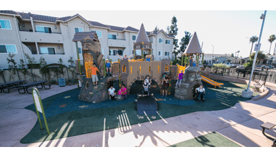 An custom all inclusive play structure disguised as a castle with ramp acting as a lowered draw bridge. Children of all ages and abilities gather and pose for a photo.