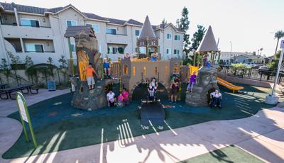 An custom all inclusive play structure disguised as a castle with ramp acting as a lowered draw bridge. Children of all ages and abilities gather and pose for a photo.