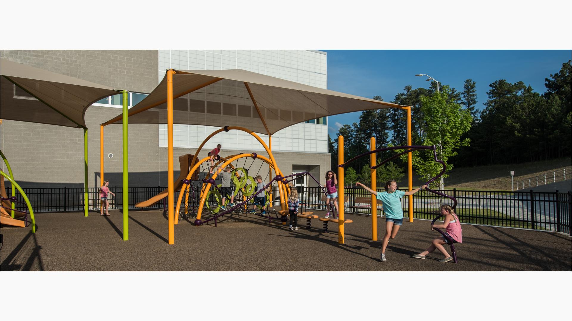 School kids playing on yellow and limon colored arched playground structure under shade structure.