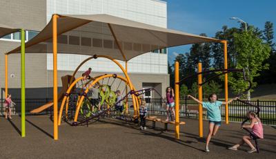 School kids playing on yellow and limon colored arched playground structure under shade structure.