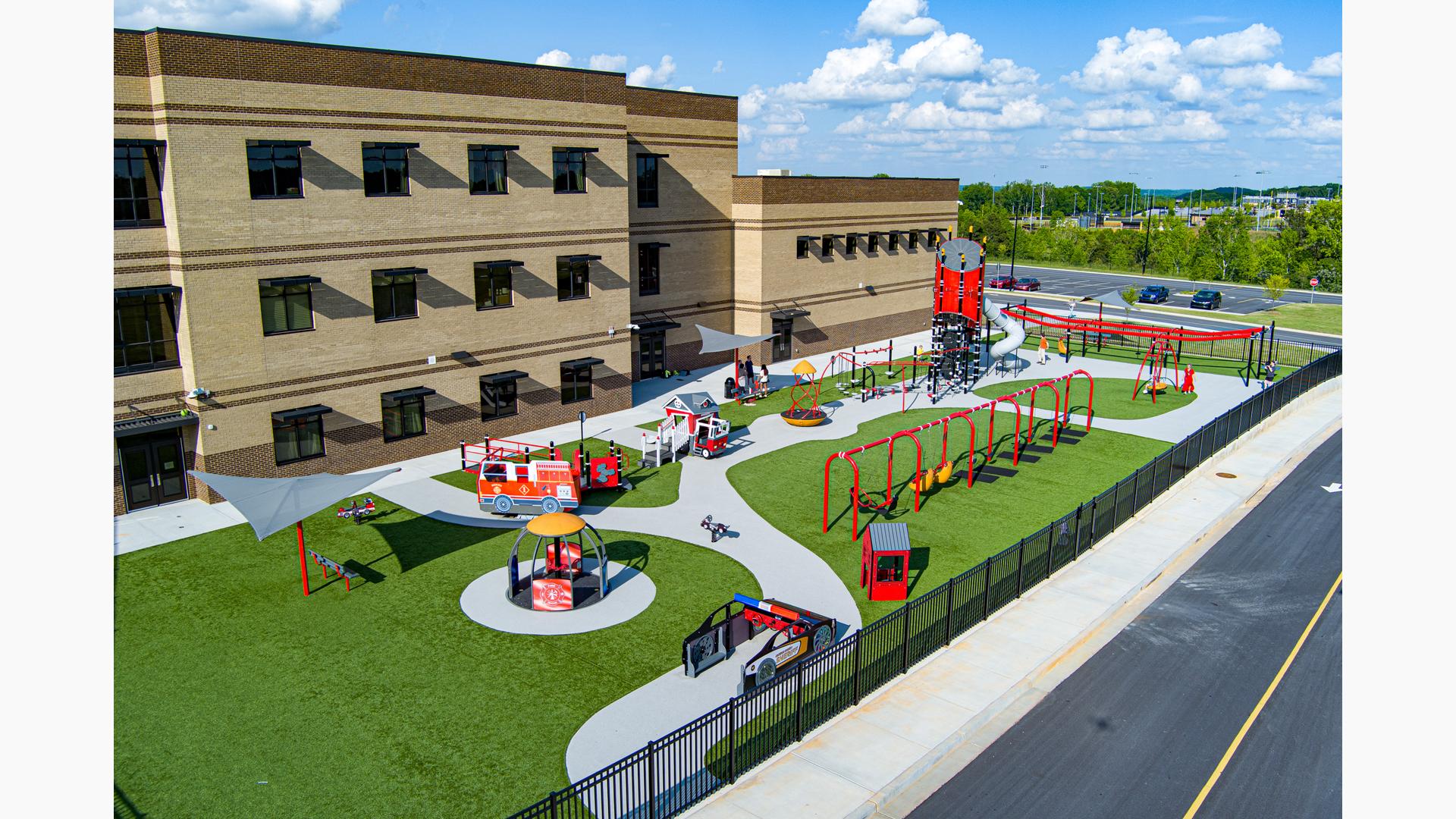 Elevated view of of a first responders themed playground outside a elementary school building.