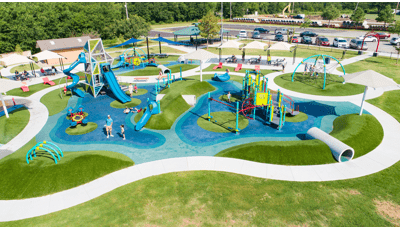 Elevated view of a outdoor unique park playground with large tower structure, smaller play area for younger children and other scattered slides, climbers and tunnels all around.