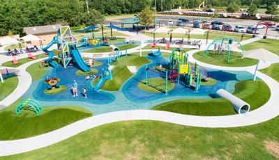 Elevated view of a outdoor unique park playground with large tower structure, smaller play area for younger children and other scattered slides, climbers and tunnels all around.