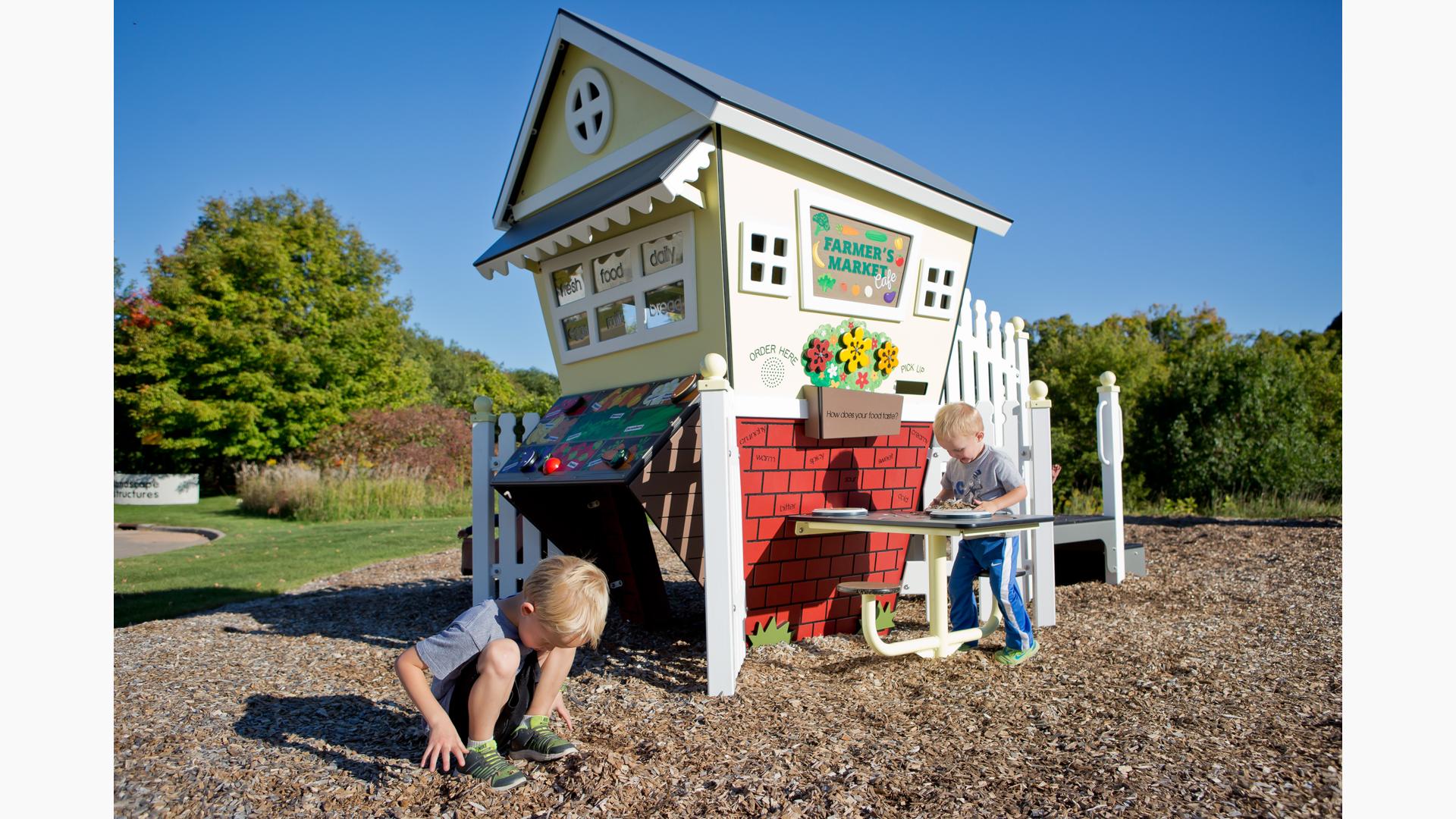 Two toddler boys playing with a playhouse farmer's market themed playground. 