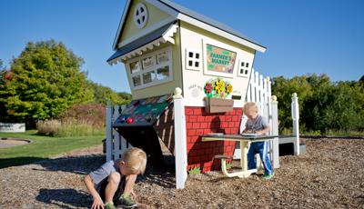 Two toddler boys playing with a playhouse farmer's market themed playground. 