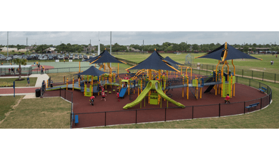 Children of all abilities at play on the Langham Creek Miracle League playground, while baseball training goes on the fields in the background.