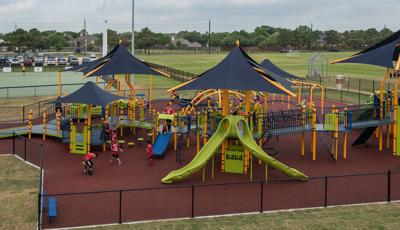 Children of all abilities at play on the Langham Creek Miracle League playground, while baseball training goes on the fields in the background.