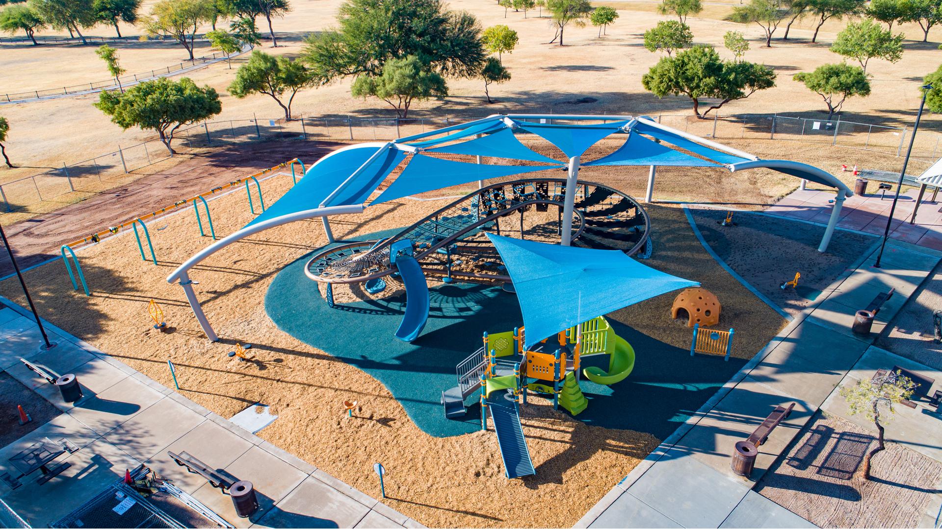 A custom blue shade structure covers a figured eight shaped play structure made up of cargo nets and belt climbers. A second playground structure with shade sits near the figure eight shaped play structure.