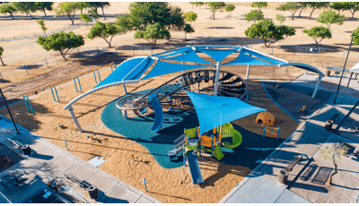 A custom blue shade structure covers a figured eight shaped play structure made up of cargo nets and belt climbers. A second playground structure with shade sits near the figure eight shaped play structure.