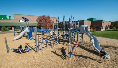 It's a sunny day at Otsego Elementary School. Children play on PlayBooster play system. Two girls sit on the Boogie Board. A boy runs past the slide, while a group of girls play on the Disc Challenge.