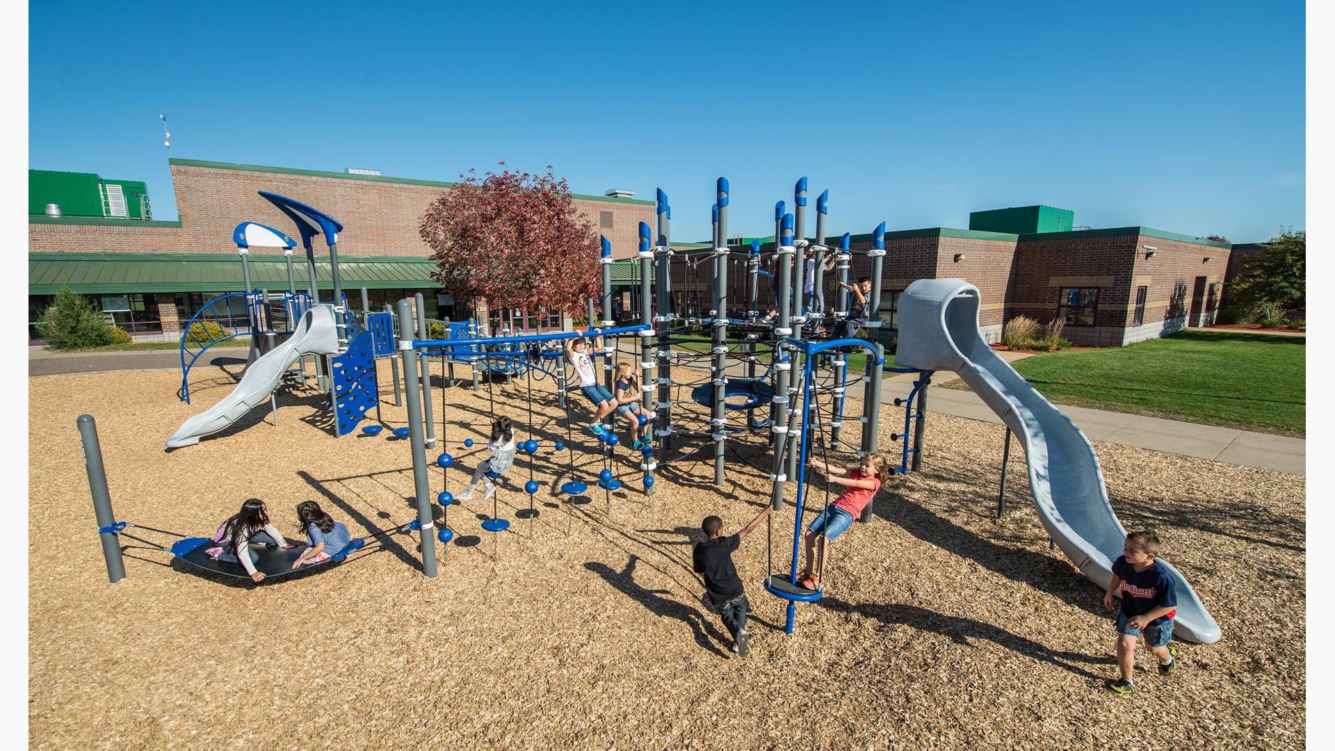It's a sunny day at Otsego Elementary School. Children play on PlayBooster play system. Two girls sit on the Boogie Board. A boy runs past the slide, while a group of girls play on the Disc Challenge.