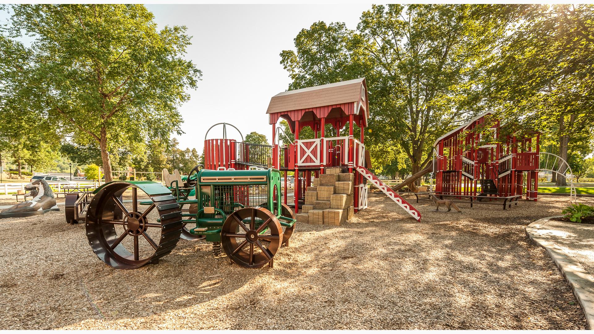 custom farm-themed playground includes a green tractor, red silo with hay barn.  And in the playground a large playground. The playground also features farm animal sculptures. 