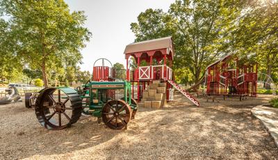 custom farm-themed playground includes a green tractor, red silo with hay barn.  And in the playground a large playground. The playground also features farm animal sculptures. 