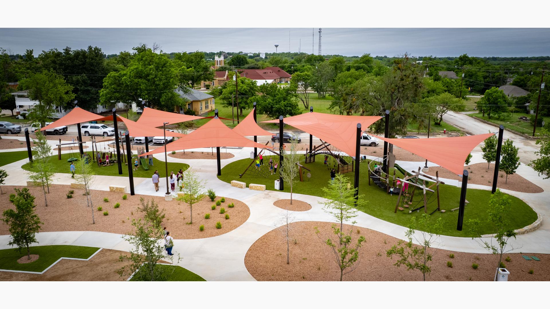 Elevated view of multiple burnt orange shade sails covering a large playground play area.