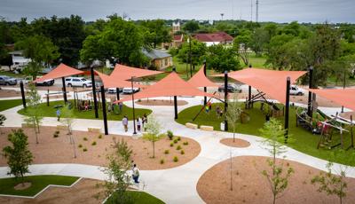 Elevated view of multiple burnt orange shade sails covering a large playground play area.
