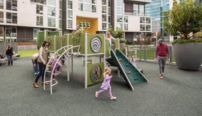 Parents watch as their toddlers run and play on the PlayShaper play structure on the rooftop of their apartment complex.