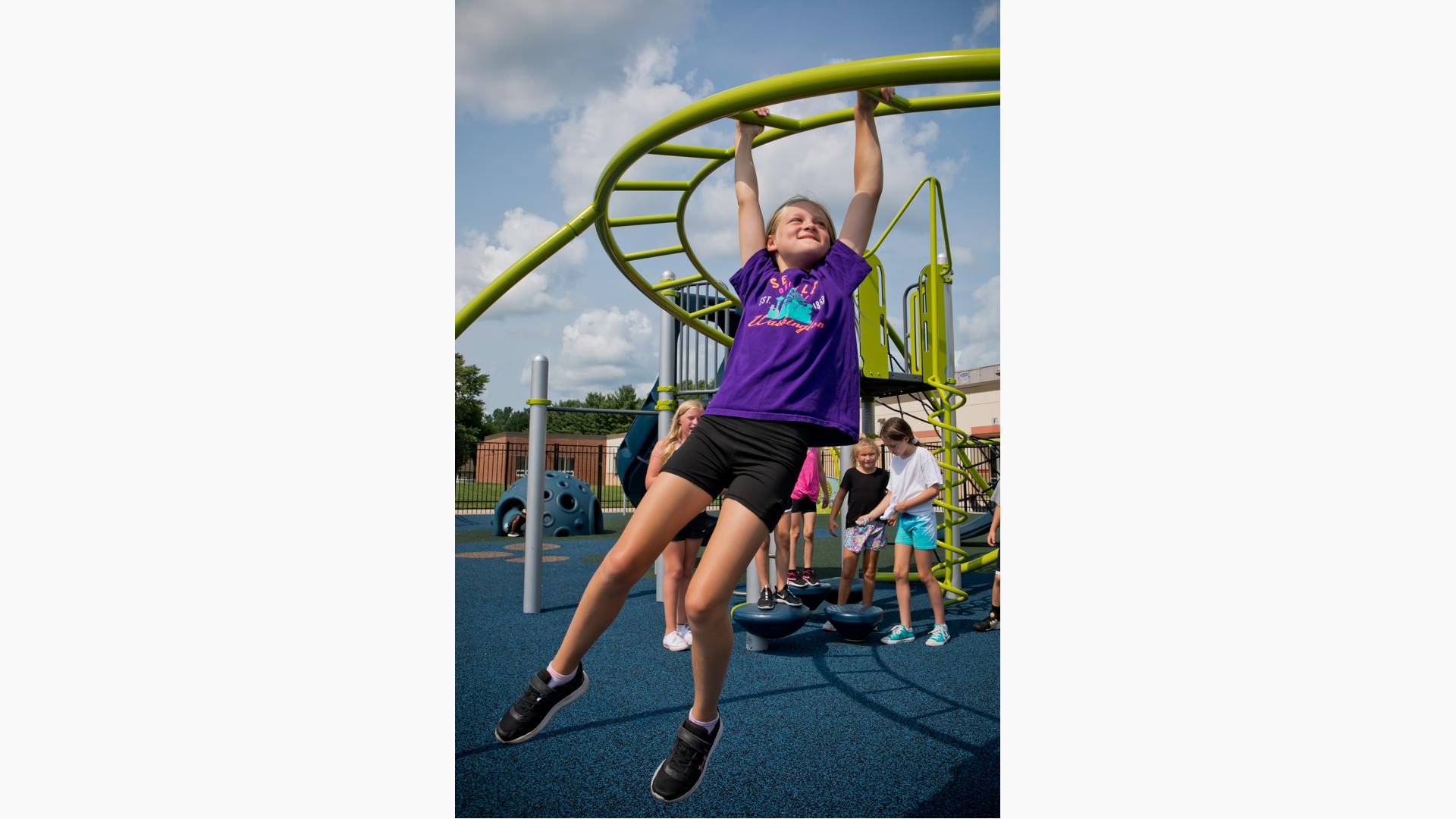 Girl smiles as she swings on Overhead Trekker™ Ladder