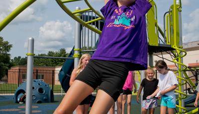 Girl smiles as she swings on Overhead Trekker™ Ladder